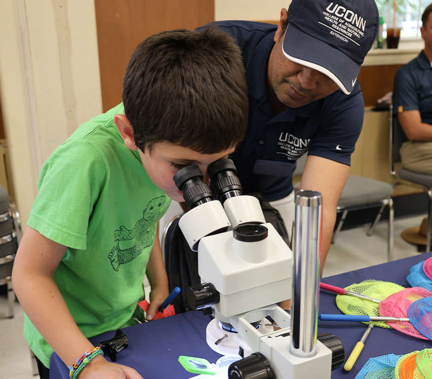 Extension educator helping a kid look through a microscope.