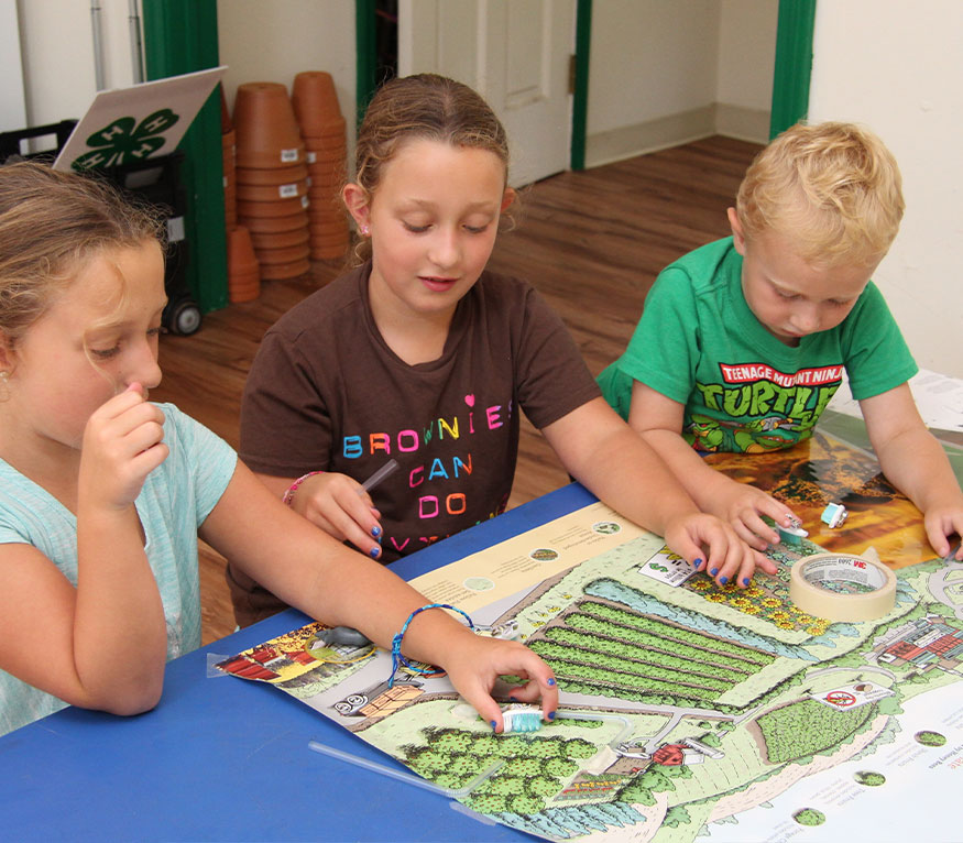 three kids at a table playing a game about bees.